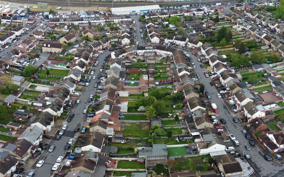 An aerial view of a densely packed residential neighbourhood showing rows of terraced houses with small gardens and backyards. Cars are parked along the narrow, winding streets that run between the ho